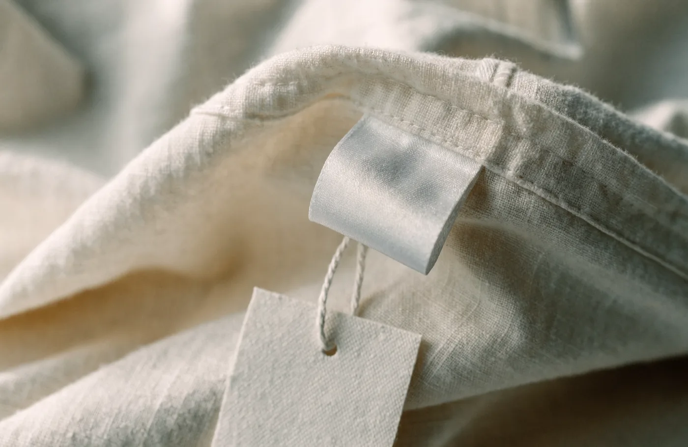 Étiquette textile vierge et carton d'accroche cousus sur un vêtement en coton naturel écru