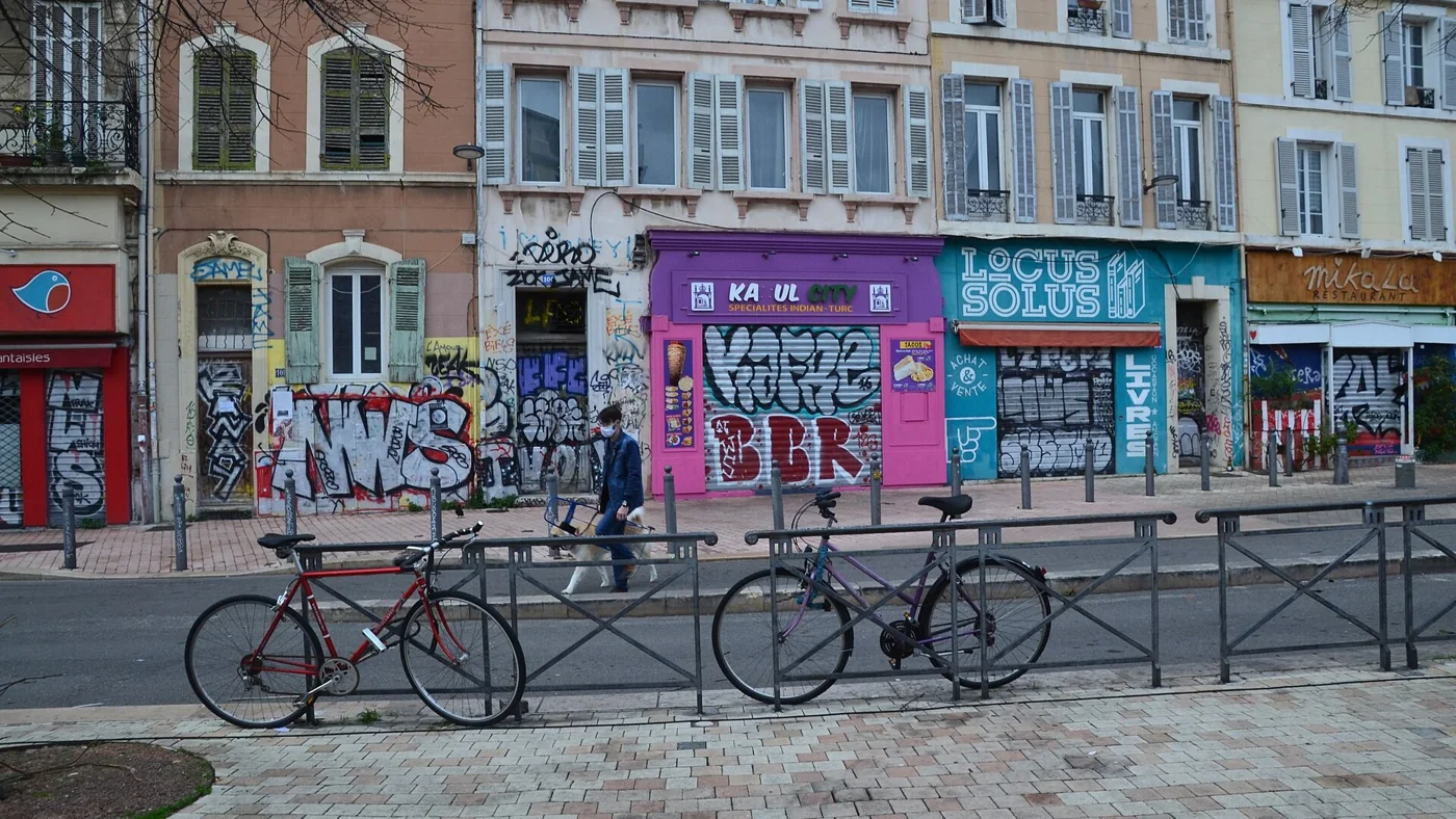 Les façades colorées du Cours Julien à Marseille, boutiques aux rideaux couverts de graffitis et vélos garés sur la place, au cœur du quartier des friperies