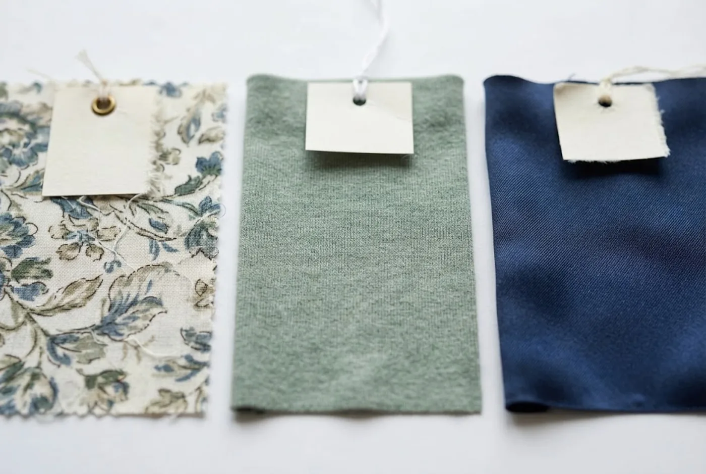 Trois échantillons de tissu alignés sur du papier blanc : viscose imprimée mate, jersey de modal doux, lyocell lisse et lustré