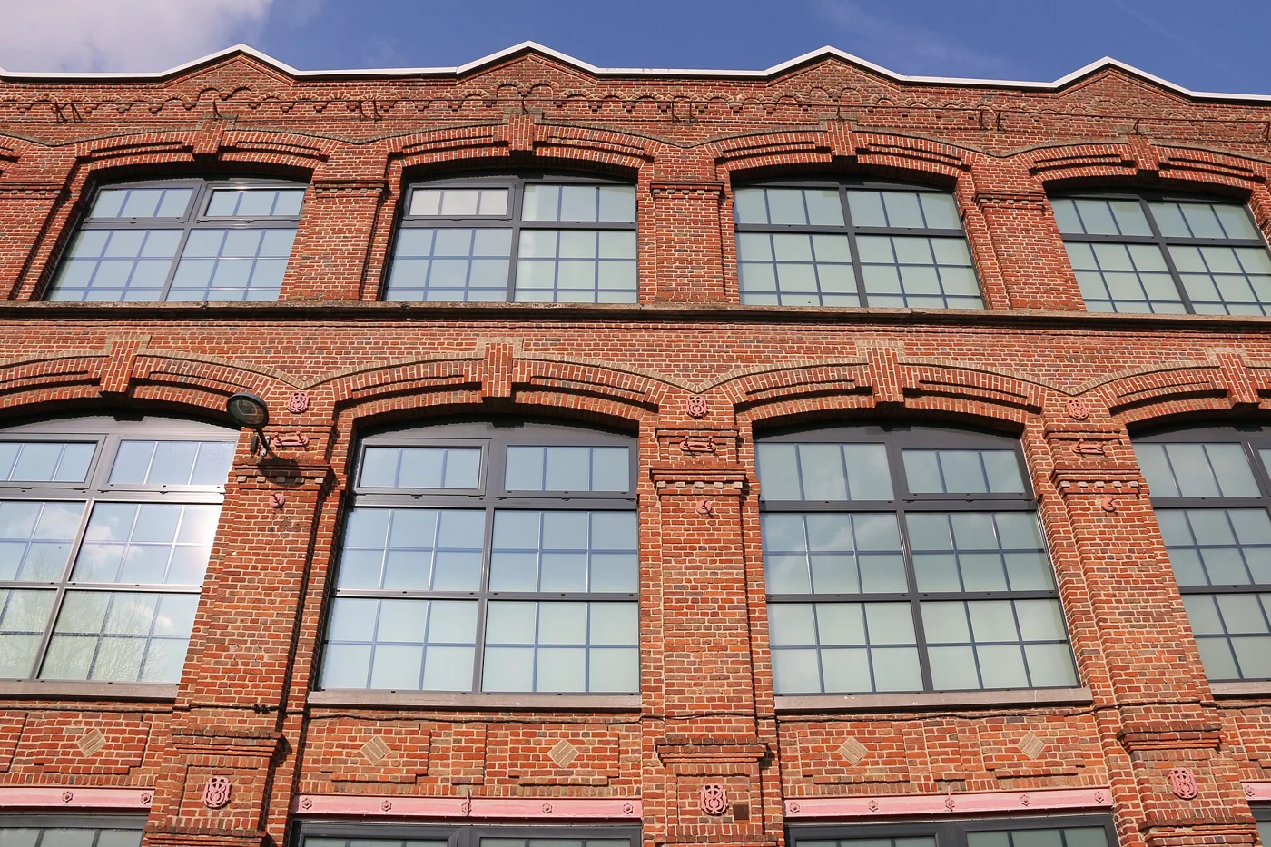La façade en brique rouge de l'ancienne usine de velours Motte-Bossut à Roubaix, avec ses grandes fenêtres cintrées et son toit en dents de scie, qui abrite aujourd'hui le centre outlet L'Usine